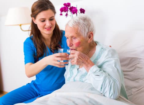 caregiver giving a glass of water to a senior woman